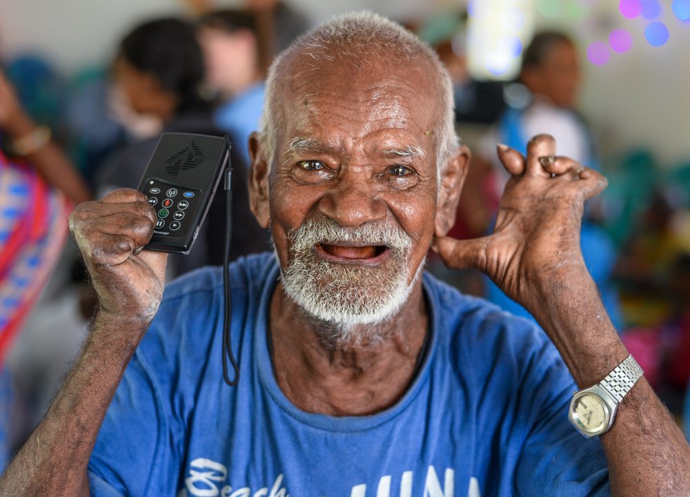 A man smiling while holding the WCOI Audio Bible device up to his ear