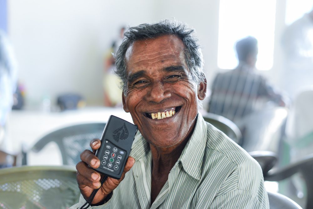 A man smiling while holding the WCOI Audio Bible device up to his ear