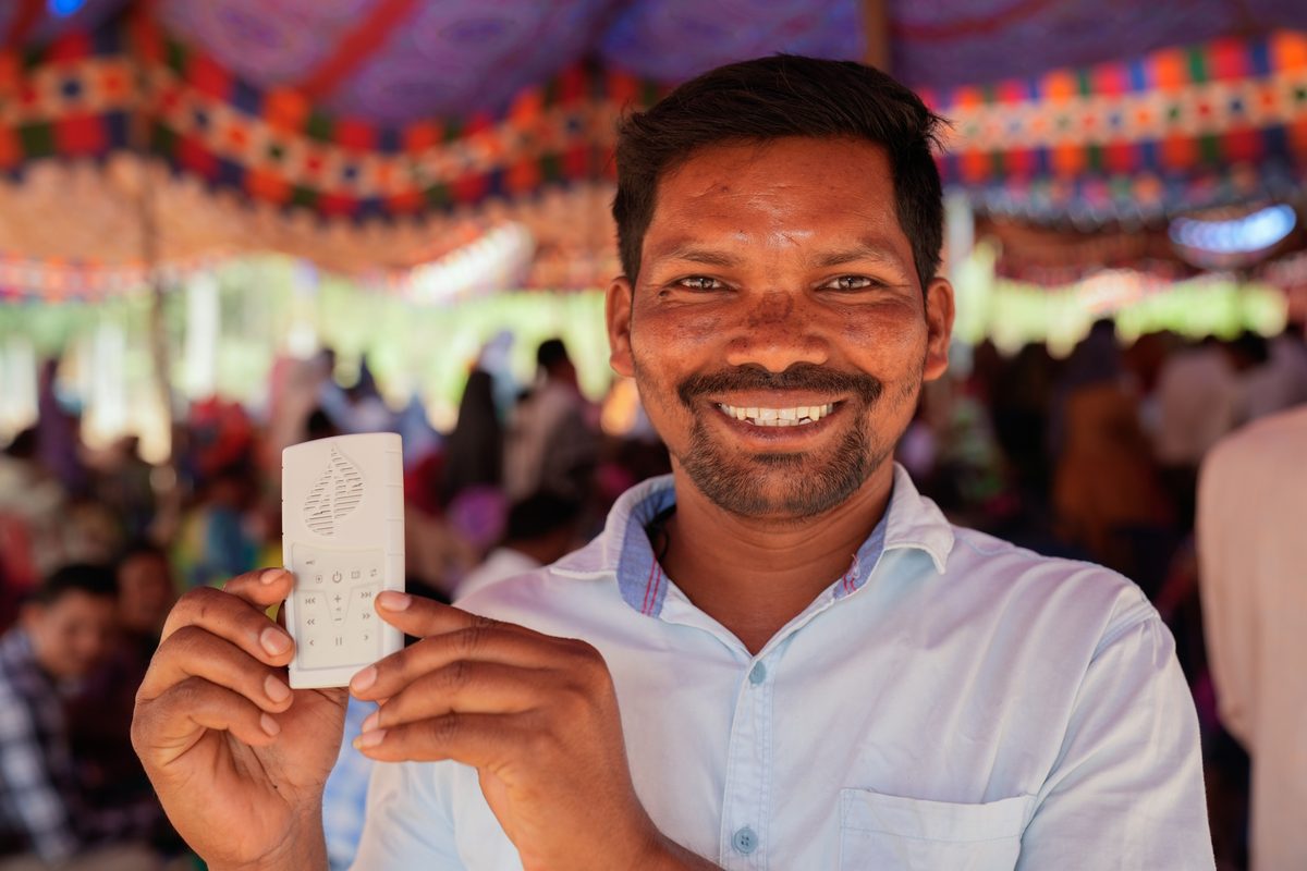 Man at an outreach event smiling while holding the WCOI Audio Bible device